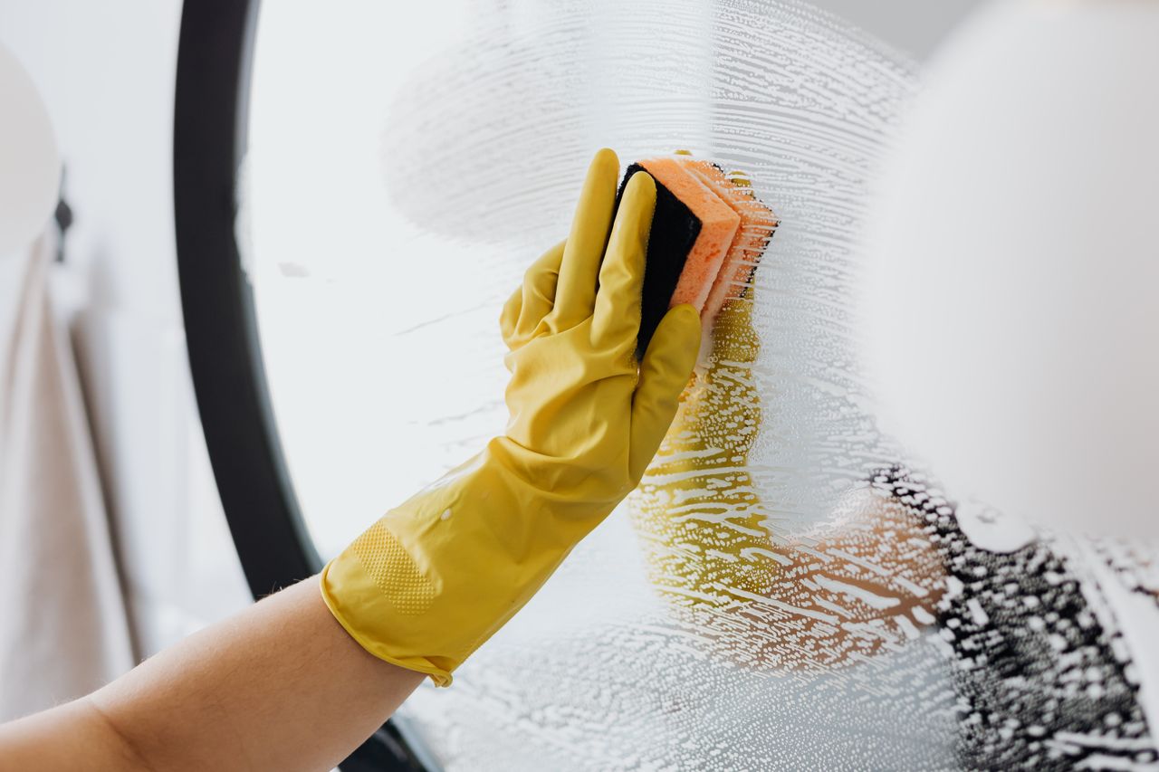 gallery-03 Anonymous person in yellow rubber gloves using a plain sponge to clean a bathroom mirror